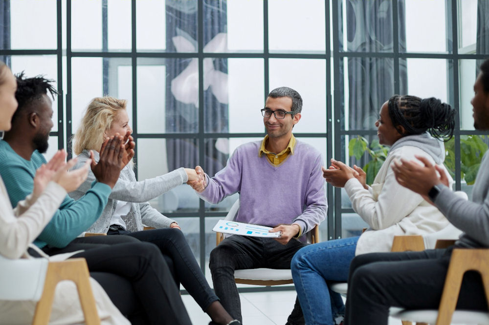 group in circle clapping for man collecting unemployment in rehab